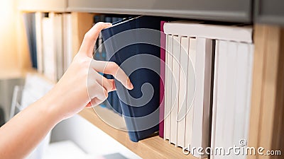 Male hand picking blue book on bookshelf Stock Photo