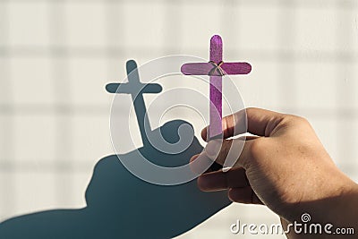 Male hand holding purple wooden cross with shadow. Christianity, faith, holy week and lent season. Stock Photo