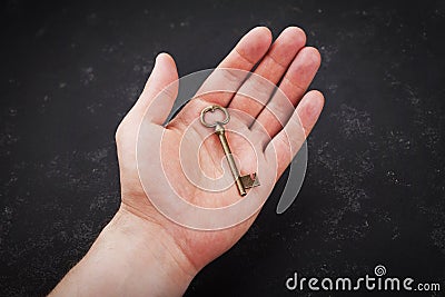 Male hand holding vintage key against black background. Stock Photo