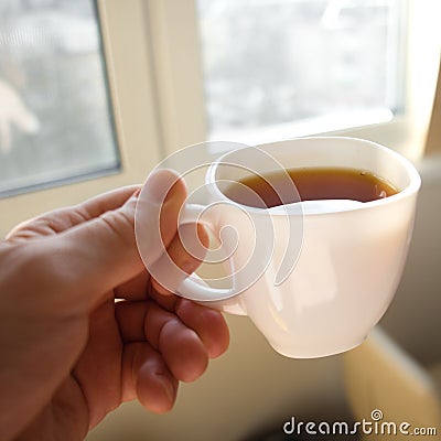 Male hand holds cup of tea in front of window. Soft focus moving action photo. Stock Photo