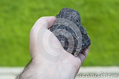 Male hand with a piece of coal on a blurred background of green forest Stock Photo
