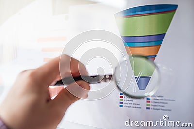 Magnifier on a coloured funnel chart printed on a white sheet of paper during a business meeting Stock Photo