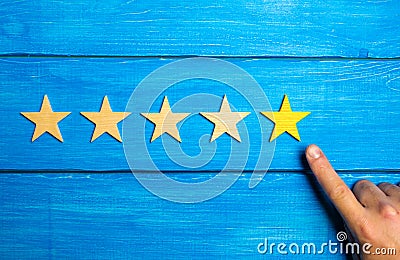 The male hand points to the fifth yellow star on a blue wooden background. Five Stars. Rating of restaurant or hotel, application. Stock Photo