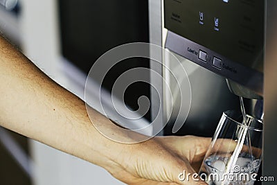 Cold water and ice cubes from dispenser of home fridge Stock Photo