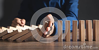 Male hand stopping falling collapse wooden block domino. Risk and Strategy Stock Photo
