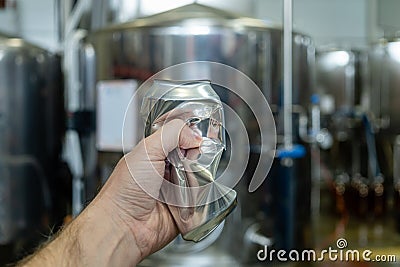 Male hand wrinkles an empty aluminum can on the background of beer equipment Stock Photo