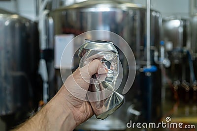 Male hand wrinkles an empty aluminum can on the background of beer equipment Stock Photo