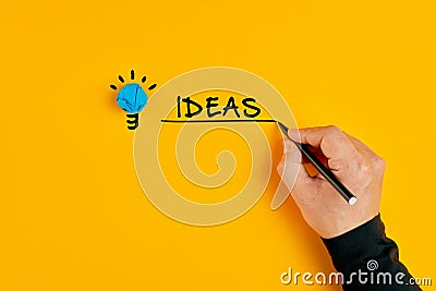 Male hand writing the word ideas next to a light bulb on yellow background Stock Photo