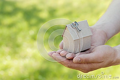 Male hands hold of cardboard house against green bokeh. Building, loan, housewarming, insurance, real estate or buying new home. Stock Photo