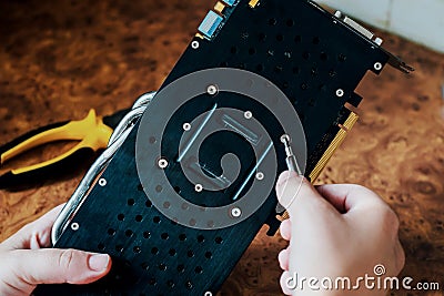 Male hands hold a screwdriver and repair computer graphics card. Stock Photo