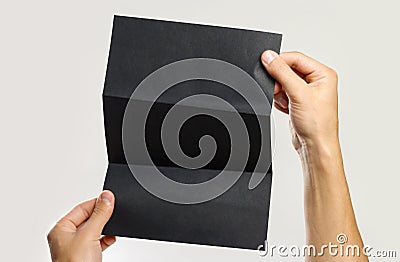 Male hands holding a black booklet triple sheet of paper. Isolated on gray background. Closeup Stock Photo