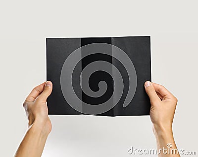 Male hands holding a black booklet triple sheet of paper. Isolated on gray background. Closeup Stock Photo