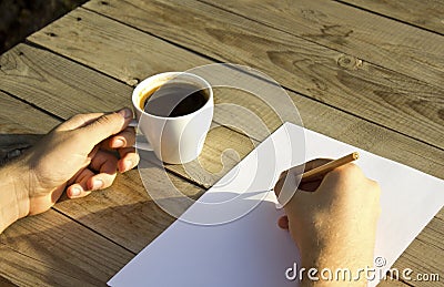 Male hands is holding coffee cup and writing on blank paper. Stock Photo