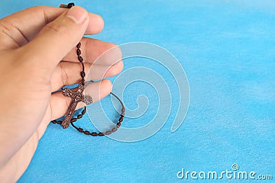 Male hands holding and praying the rosary or scapular in sky blue background. Stock Photo
