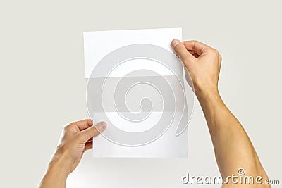 Male hands holding a white booklet triple sheet of paper. Isolated on gray background. Closeup Stock Photo