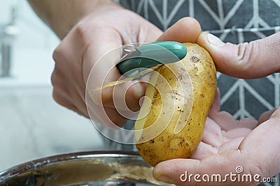 Male hands peeling fresh potato with peeler over bowl closeup. Food scrap, separate waste collection, zero waste. Stock Photo