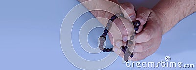 Male hands praying holding a wooden rosary as symbol of Christianity, faith and spirituality Stock Photo