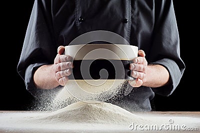 Male hands sifting flour from old sieve on old wooden kitchen table. on black background. Stock Photo