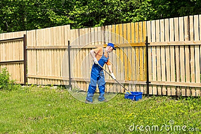 Male handyman wearing blue overalls paints wooden fence Stock Photo