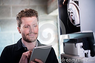 Male Heating Engineer Working On Central Heating Boiler Using Digital Tablet Stock Photo