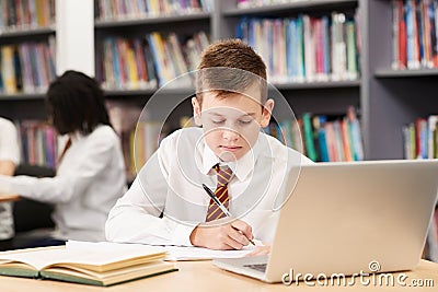 Male High School Student Wearing Uniform Working At Laptop In Li Stock Photo