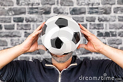 Male holding a soccer ball in front of his face against a grey cobblestone wall Stock Photo