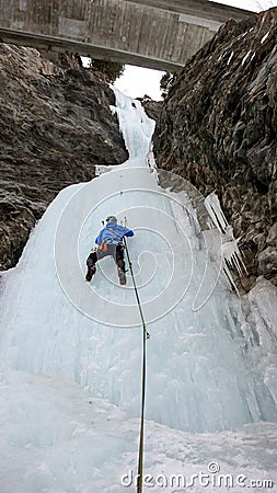 Male ice climber in a blue jacket climbs a frozen waterfall in the Avers Valley in the Swiss Alps Stock Photo