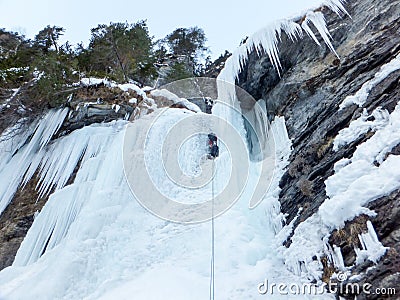 Male ice climber on the last pitch of a very hard and steep ice fall in a narrow rock gully in the Alps Stock Photo