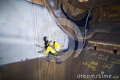 Male industrial rope access technician painter working at height hanging on twin ropes Stock Photo