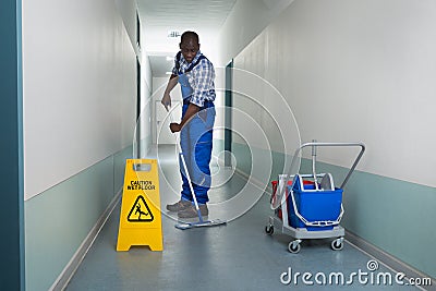 Male Janitor Mopping In Corridor Stock Photo