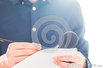 Male journalist at news conference, holding microphone and taking notes Stock Photo