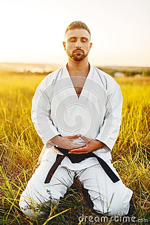 Male karate fighter sitting on the ground in field Stock Photo