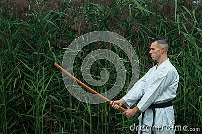 Male karate in a traditional kimono with a black belt practices karate kick with a bokken. Stock Photo