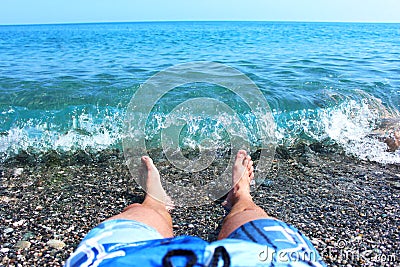 Male legs while sunbathing, lying carefree in the water on pebbles near the coastline Stock Photo