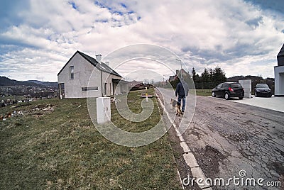 A male man with a german shepherd dog is walking on the side of the road in a country side. Rear view. a loyal friend of man. Stock Photo