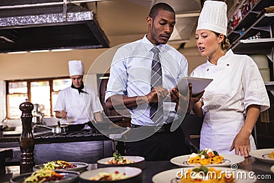 Male manager and female chef using digital tablet in kitchen Stock Photo