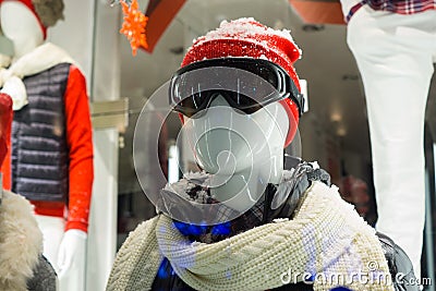 Male mannequin in store window during winter with ski gear, woolly hat, dark goggles, scarf, down jacket and fake snow on head Stock Photo