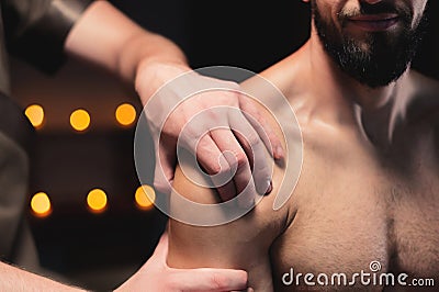 Male masseur doing sports massage in luxury spa salon to male athlete with a beard on the background of burning candles Stock Photo