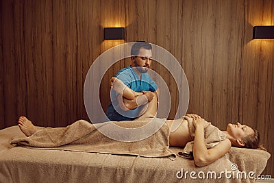 Male masseur rubbing leg to slim woman, massage Stock Photo
