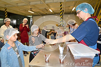 Male master hands out chocolate mass to children for tasting. Children `s tour to the Belgostar chocolate factory Editorial Stock Photo