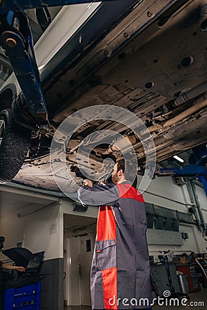 Mechanic under car in garage examing tire and technical condition Stock Photo