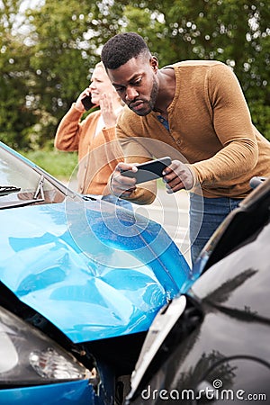 Male Motorist Involved In Car Accident Taking Picture Of Damage For Insurance Claim Stock Photo