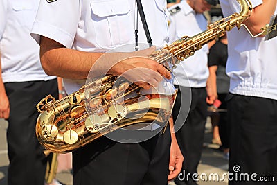 A male musician in a white shirt holds a large beautiful golden saxophone in a column of military musicians, close-up Stock Photo