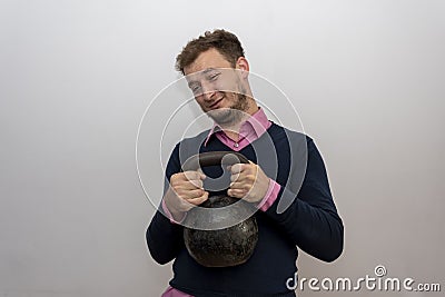 A male nerd 35-38 years old is trying to lift a heavy weight on a light background. Stock Photo
