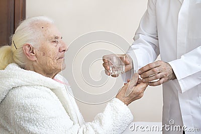 Male nurse gives a glass of medicines and a glass of water to an old woman. Stock Photo