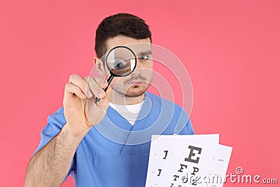 Male nurse holds magnifier and vision test on pink background Stock Photo