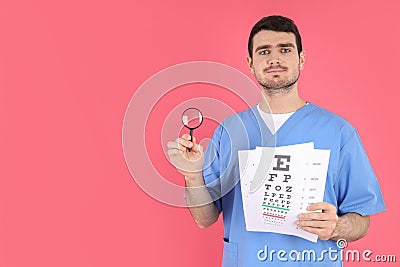 Male nurse holds magnifier and vision test on pink background Stock Photo