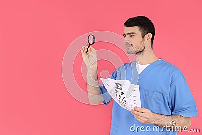 Male nurse holds magnifier and vision test on pink background Stock Photo