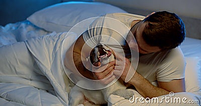 Male owner is inspecting teeth of his jack russell puppy, lying in bed at night Stock Photo