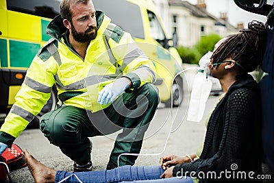 Male paramedic putting on an oxygen mask to an injured woman on a road Stock Photo